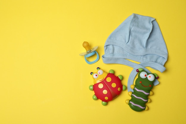 Gorro de bebé y juguetes sobre fondo amarillo.