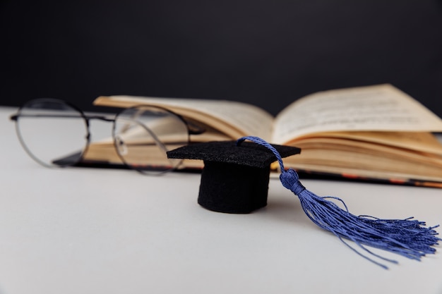 Gorro de graduación y vasos con libro abierto sobre una mesa. Centrarse en el sombrero.