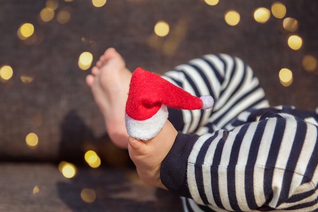 Gorro de Papá Noel al pie del bebé con luces decorativas en el fondo