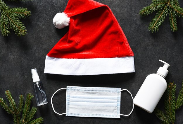 Gorro de Papá Noel, máscara médica y antiséptico sobre un fondo de hormigón negro.