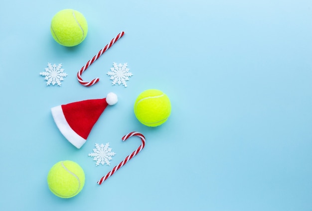 Gorro de Papá Noel, pelotas de tenis, bastones de caramelo y copos de nieve sobre fondo azul.