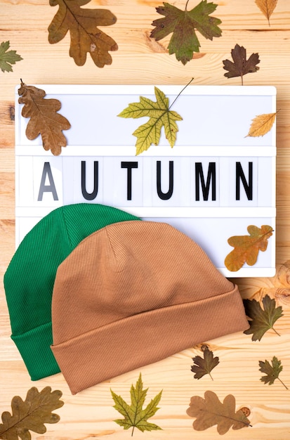 Gorros Beanie con la inscripción Otoño con hojas amarillas en una mesa de madera Anuncio de la tienda