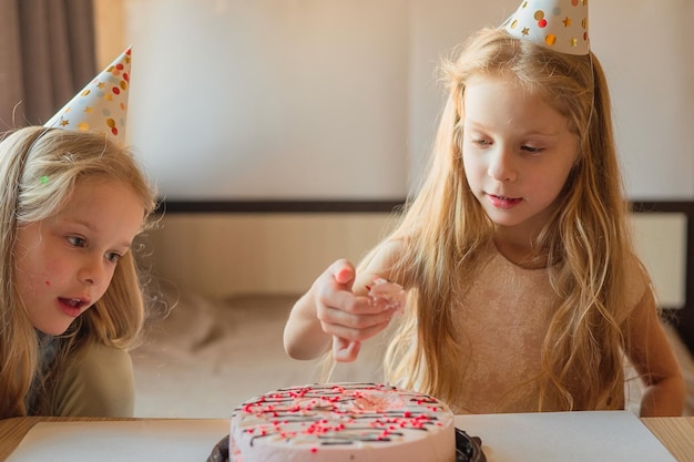 Gorros directos para niños y niñas sin dudarlo comen un hermoso pastel de cumpleaños con sus manos en casa cumpleaños de niños durante el aislamiento de cuarentena por enfermedad