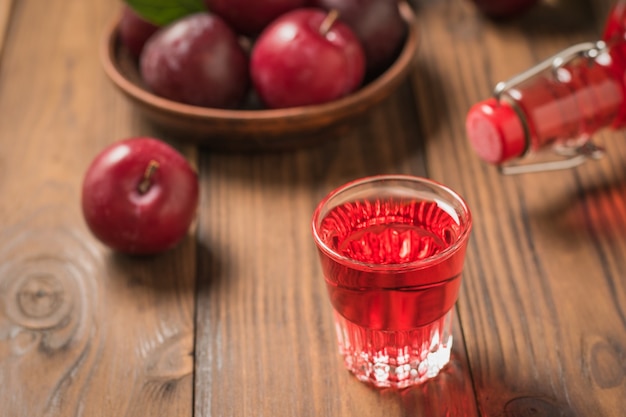 Goss ein Glas Pflaumenlikör, eine Flasche und reife Beeren auf einen Holztisch. Hausgemachtes alkoholisches Getränk aus Beerenpflaumen. Der Blick von oben.