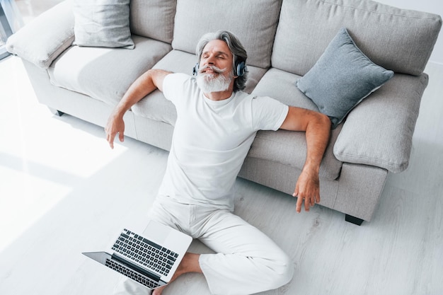 Gosta de música Homem moderno elegante sênior com cabelos grisalhos e barba dentro de casa