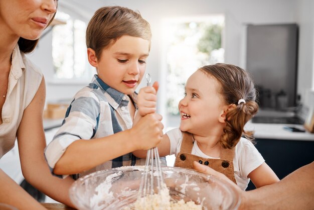 Gostamos de ajudar na cozinha. Foto de dois irmãos assando juntos em casa com a ajuda de sua mãe.