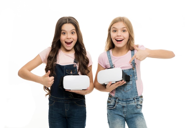 Gostamos deste jogo. Crianças felizes gostam de jogar videogame juntos. Meninas pequenas apontando para fones de ouvido vr e dando sinal de polegar de semelhante. Perfeito, se você também gostar.