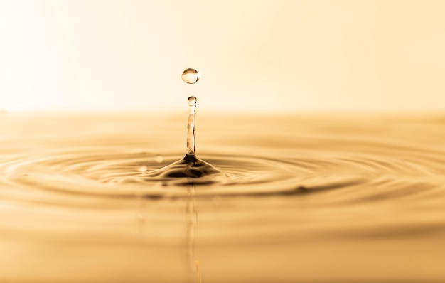 Foto gota de agua gota de agua transparente con ondas circulares gotas de agua salpicadas de amarillo dorado ligeramente borrosas concepto de gota de agua natural y utilícelo como fondo