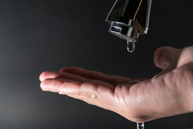 Gota de agua en el grifo con fondo negro