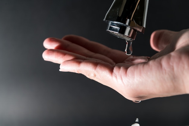 Gota de agua en el grifo con fondo negro