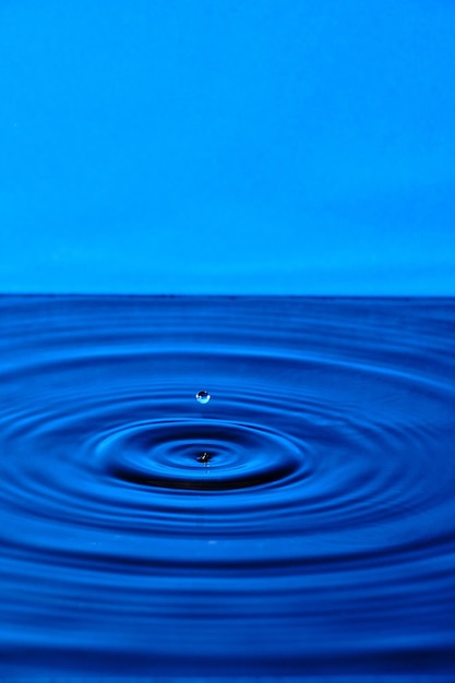 Gota de agua salpicada con círculos de agua divergentes sobre fondo azul