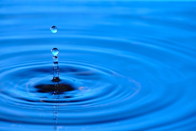 Gota de agua salpicada con círculos de agua divergentes sobre fondo azul