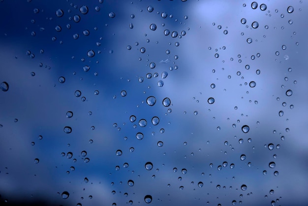 Gota de água de tamanho misto em um vidro de janela com céu azul de nuvens ao fundo