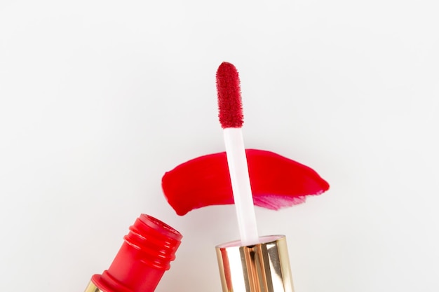 Gota de batom líquido vermelho manchada em um fundo branco Brilho labial vermelho em um tubo com um aplicador