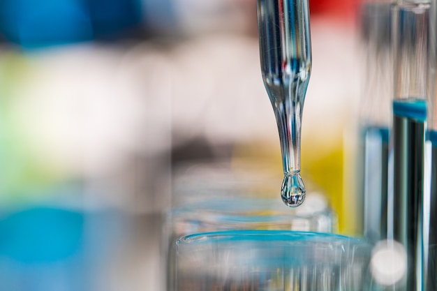 Foto gota de líquido azul de droper caindo para tubo de ensaio em laboratório com fundo de desfoque de cor brilhante. conceito de extrato puro e limpo.