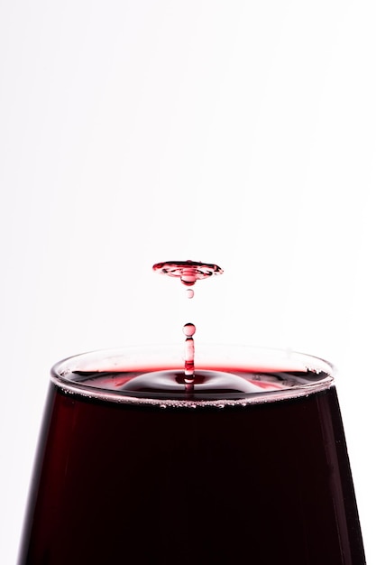 Gota de vinho tinto caindo em um copo isolado em branco close upxA