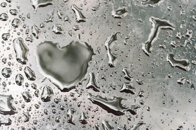 Gota en forma de corazón sobre vidrio húmedo gris