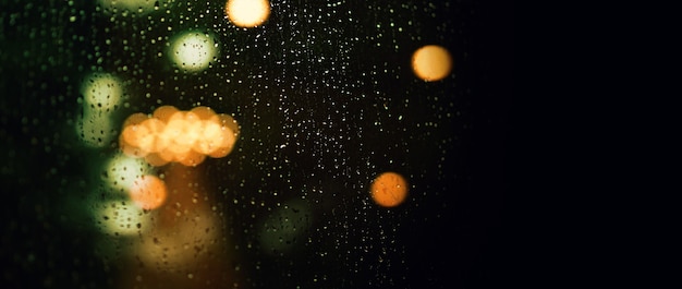 Gota de lluvia en la ventana por la noche. Ventana de la sala de estar del condominio o apartamento en la noche de la temporada de lluvias en Bangkok, Tailandia. La ventana exterior es un bokeh borroso de llover la luz de la ciudad y el árbol y el cielo naturales.