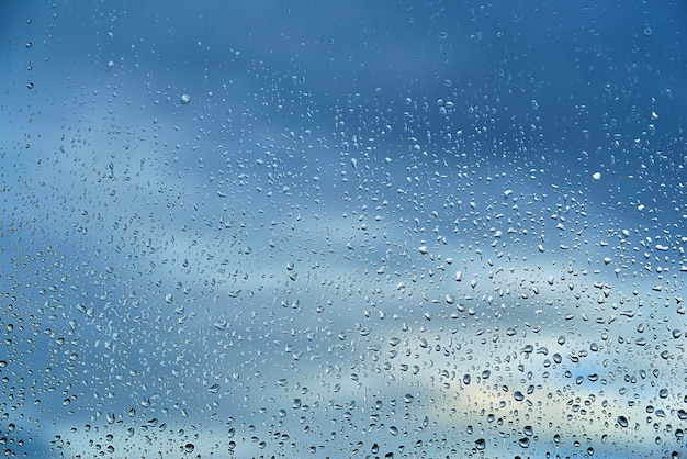 Gotas abstratas de água no vidro da janela em um borrão de um céu azul nublado para plano de fundo texturizado