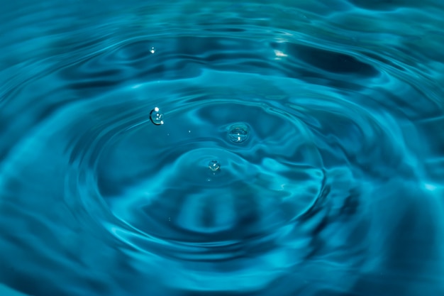 Gotas de agua caen en la superficie del agua que causa una ondulación azul.