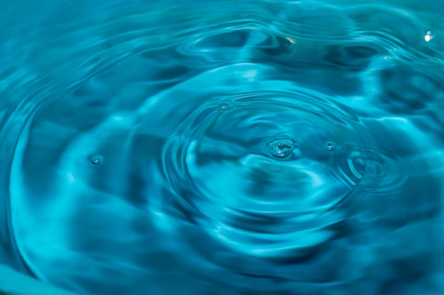 Gotas de agua caen en la superficie del agua que causa una ondulación azul.