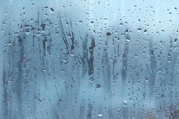 Gotas de agua corren por el cristal empañado con un fondo borroso