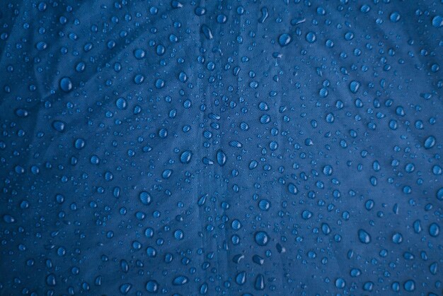 Gotas de agua de lluvia sobre un fondo azul hecho de tela impermeable Textura y fondo abstracto