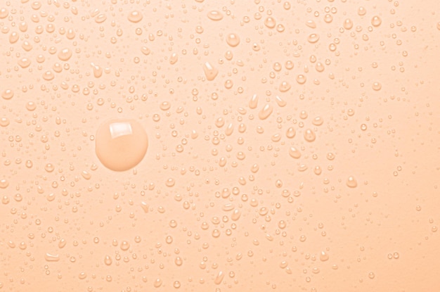 Gotas de agua micelar o tónico cosmético sobre un fondo naranja Fotografía macro de primer plano