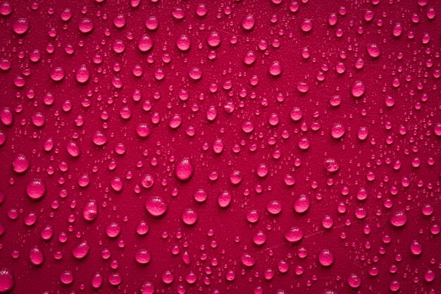 Gotas de agua sobre la superficie de color rojo oscuro. Foto macro, gota, base de plástico de sombra.