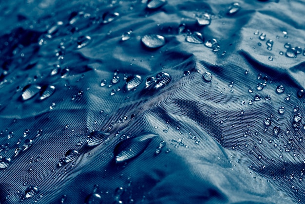 Gotas de agua sobre tejido de membrana impermeable. Vista detallada de la textura de la tela impermeable azul.