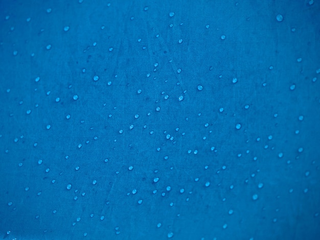 Gotas de agua sobre tejido de membrana impermeable. vista detallada de la textura de la tela impermeable sintética azul. rocío de la mañana en la tienda.