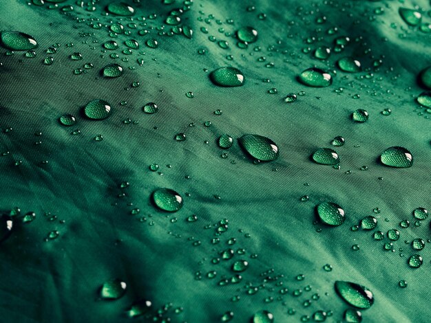 Gotas de agua sobre tejido de membrana impermeable. Vista detallada de la textura de la tela impermeable verde.