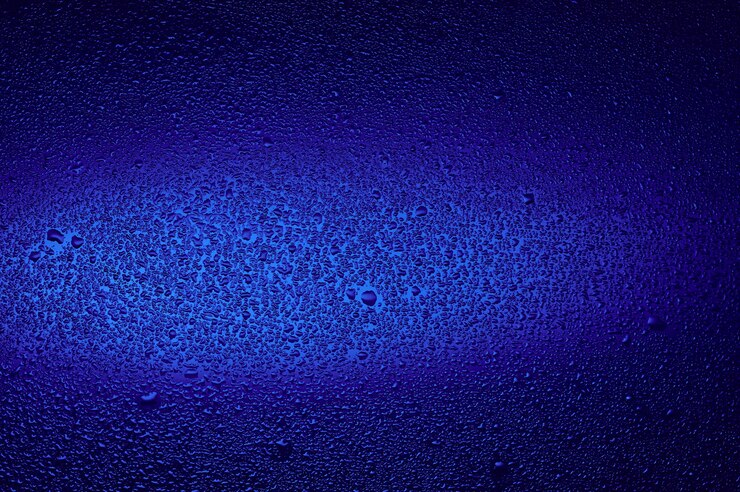 Gotas de agua sobre vidrio negro. Fondo iluminado con azul oscuro