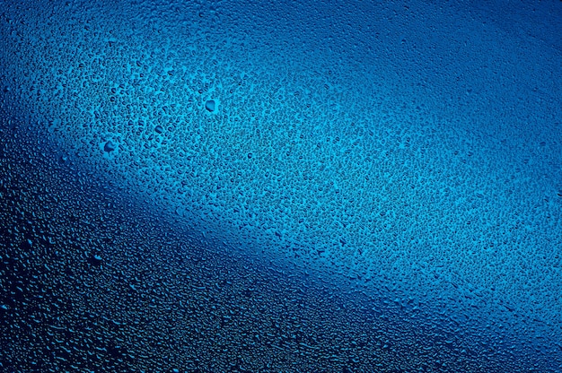 Gotas de agua sobre vidrio negro. Fondo iluminado con azul