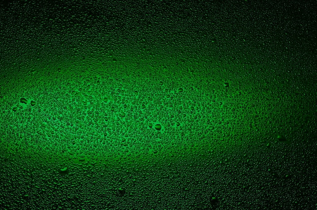 Gotas de agua sobre vidrio negro. Fondo iluminado con verde