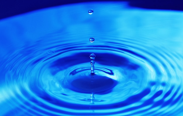 Gotas cayendo en el agua y círculos caminando sobre el agua, con reflejo. Fondo azul, textura