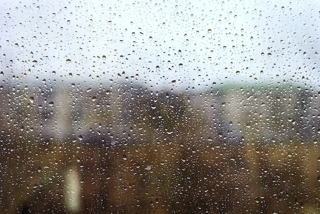 Foto gotas de água da chuva no vidro da janela contra a paisagem urbana, matizada