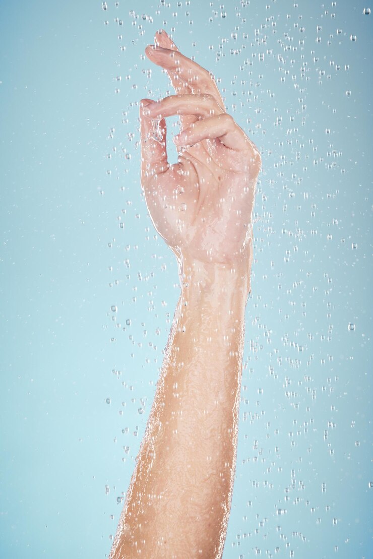 Foto gotas de água mão e close-up com chuveiro de limpeza e dermatologia matinal em estúdio braço de pessoa de fundo azul e respingo para lavagem de bem-estar e brilho da pele com autocuidado e segurança de higiene