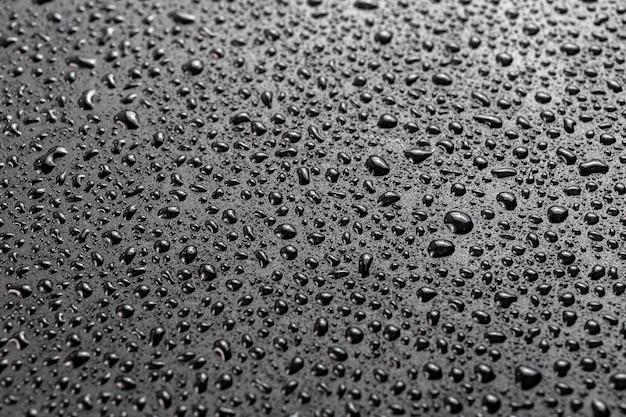 Gotas de água no fundo macro de superfície hidrofóbica preta plana abstrata com foco seletivo