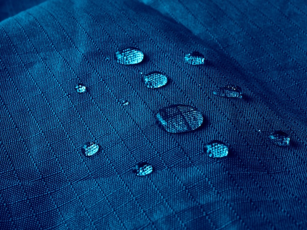 Gotas de água no tecido da membrana impermeável. Visualização de detalhes da textura de um pano impermeável azul.