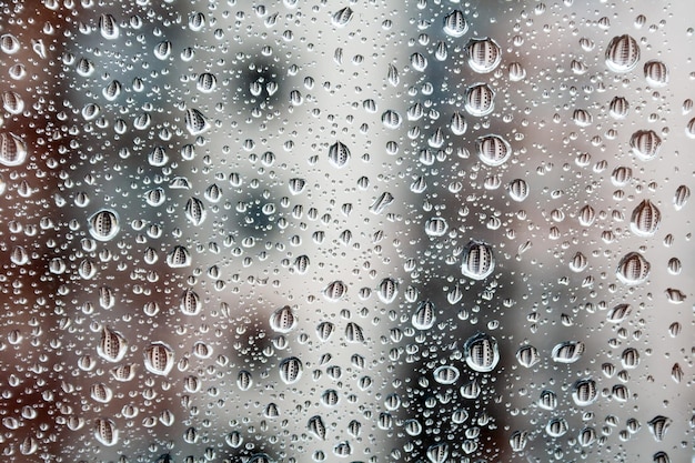 Gotas de água no vidro da janela contra um fundo desfocado de uma casa em um dia nublado chuvoso Gotas de tamanhos diferentes refletem o prédio vizinho