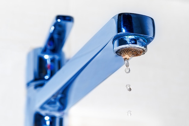 Foto gotas de água pingam da torneira cromada da pia da cozinha ou do banheiro. o conceito da ideia de economia de água.