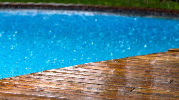 Gotas de chuva caem em um terraço de madeira e uma ponte perto da piscina close-up