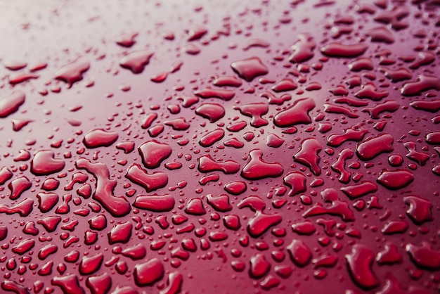 Gotas de chuva molhadas no capô vermelho do carro Fundo abstrato Gotas de água na textura de metal vermelho Corpo do carro de foco raso Detalhe da superfície molhada vermelha após a chuva