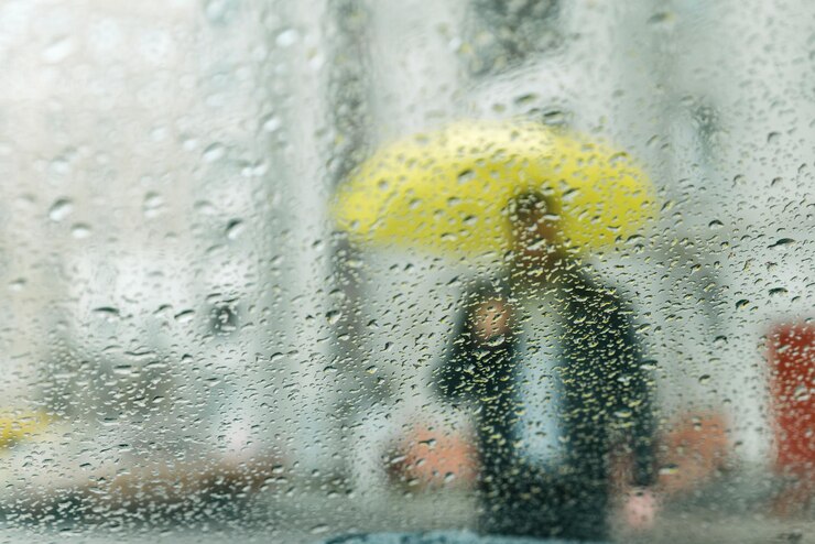 Foto gotas de chuva molhadas no vidro. homem com silhueta amarela através de vidro molhado