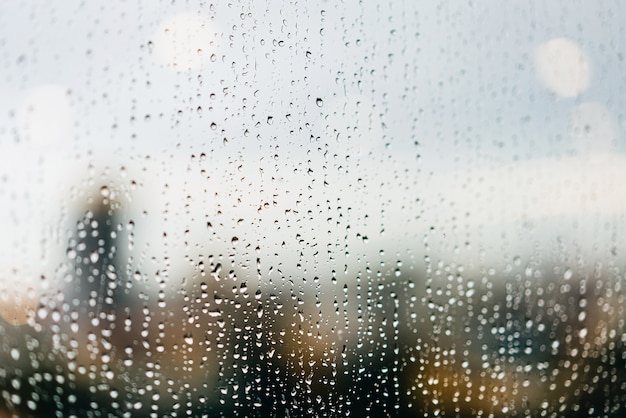 Gotas de chuva nas janelas de vidro no crepúsculo com os semáforos refletidos e desfocam edifícios altos ao fundo.