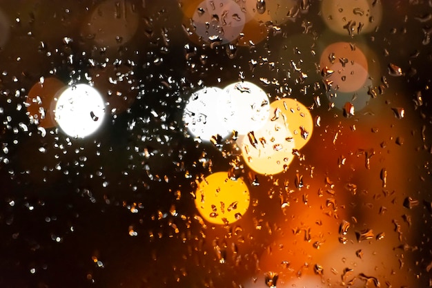 Gotas de chuva no vidro ao fundo desfocam as luzes da cidade desfocadas