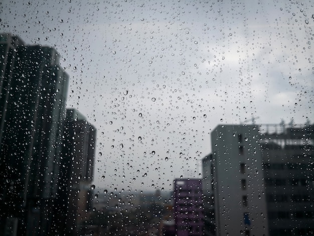 Gotas de chuva no vidro da janela com edifício turva do arranha-céu na cidade.