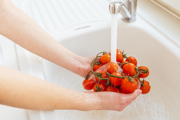 Gotas de jato de água fluem de tomates vermelhos maduros, mãos femininas lavam legumes frescos