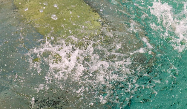 Gotas frecuentes de agua en una fuente a cámara lenta caen sobre una superficie de agua limpia con salpicaduras y burbujas. Chorros de agua brillan al sol. El aerosol se extiende lentamente hacia los lados. De cerca.